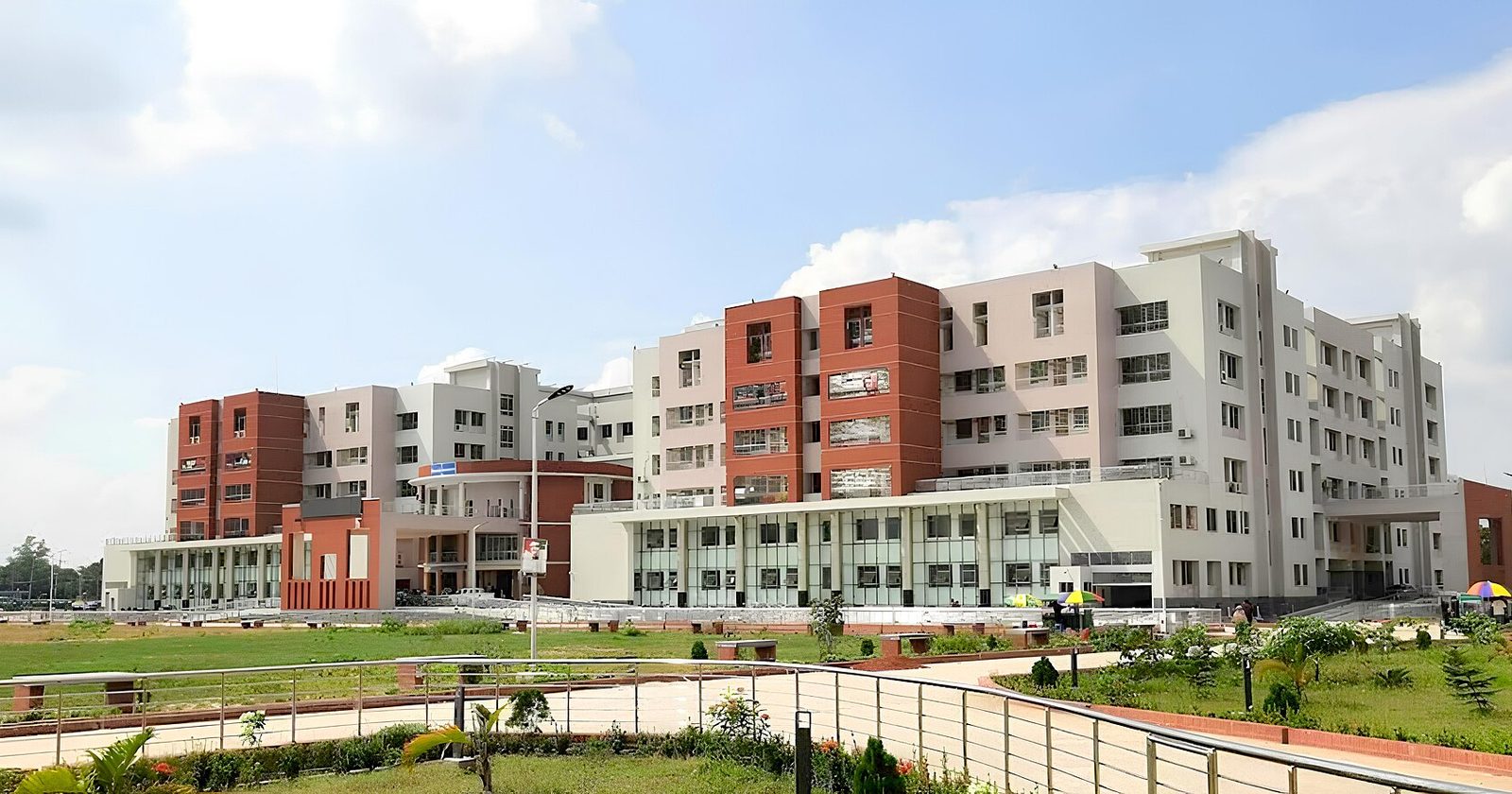 Duży, nowoczesny wielopiętrowy kompleks szpitalny z biało-ceglaną elewacją, otoczony zielenią pod błękitnym niebem