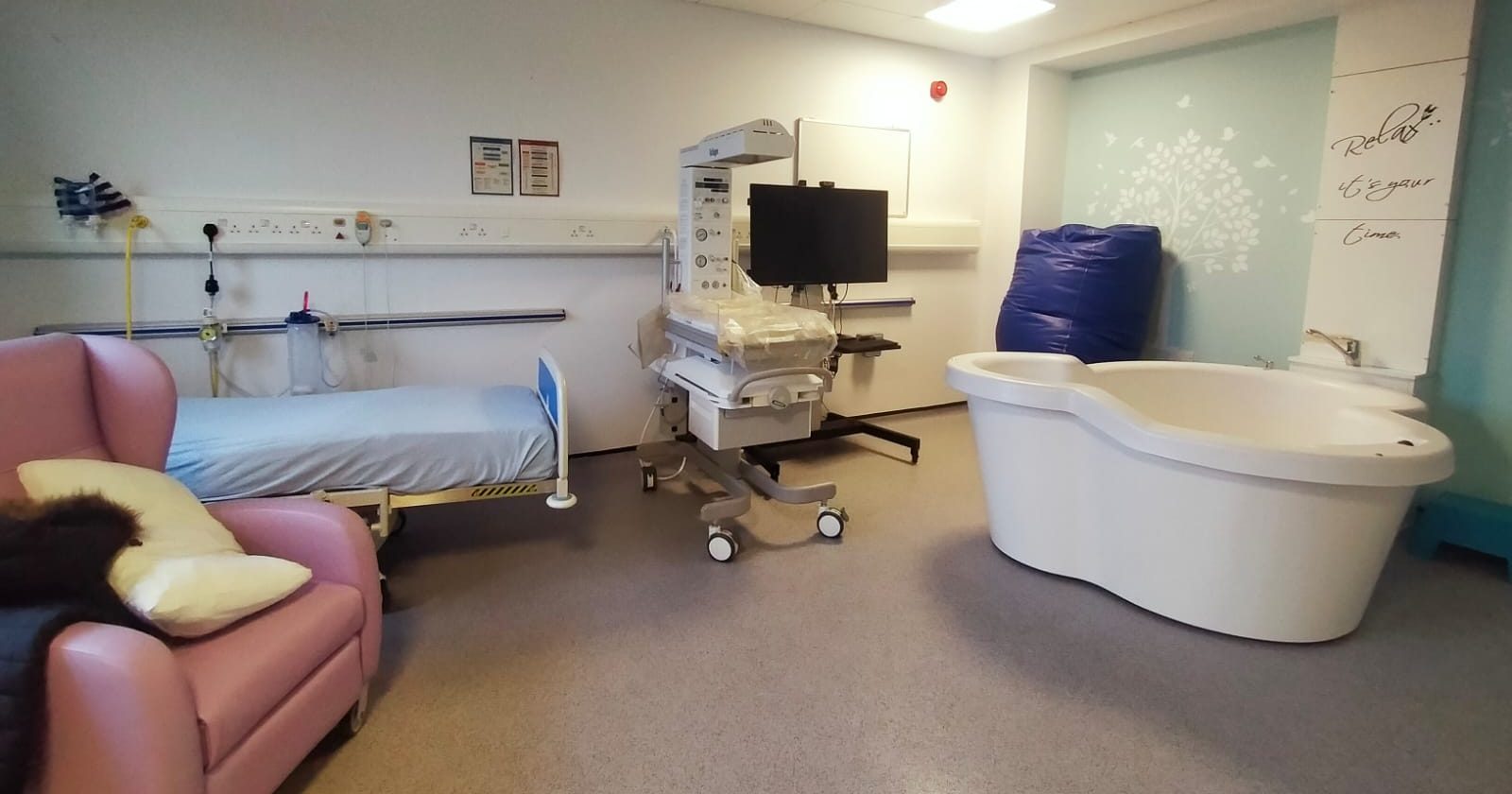 Sala porodowa w niewielkim szpitalu — łóżko, stanowisko noworodkowe i wanna do porodu w wodzie