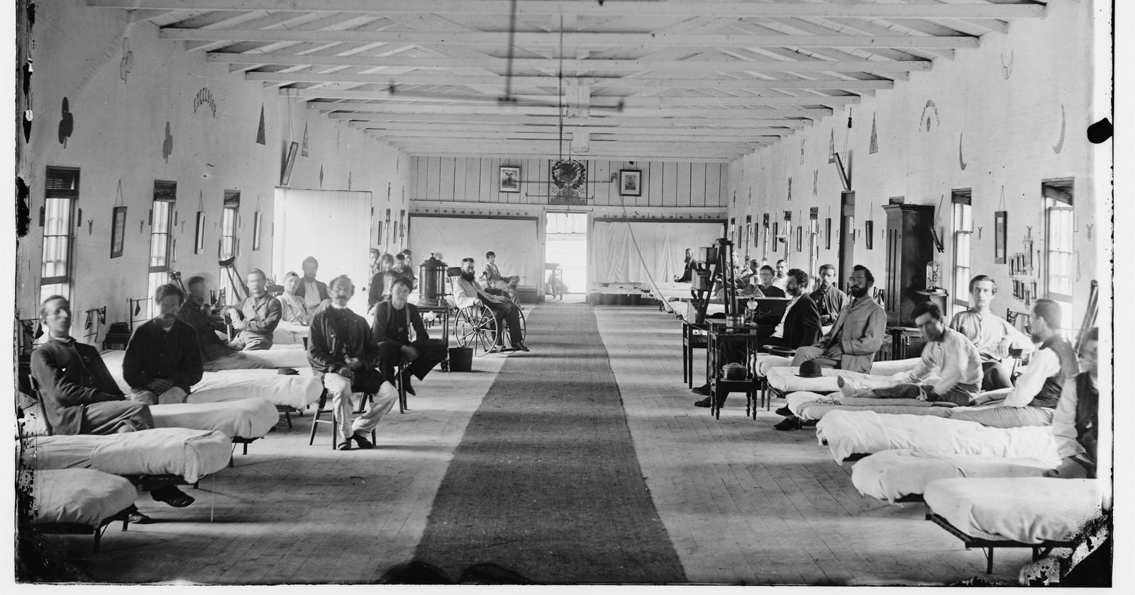 Długa sala historycznego szpitala z rzędami łóżek — chłodna, instytucjonalna przestrzeń publicznej ochrony zdrowia